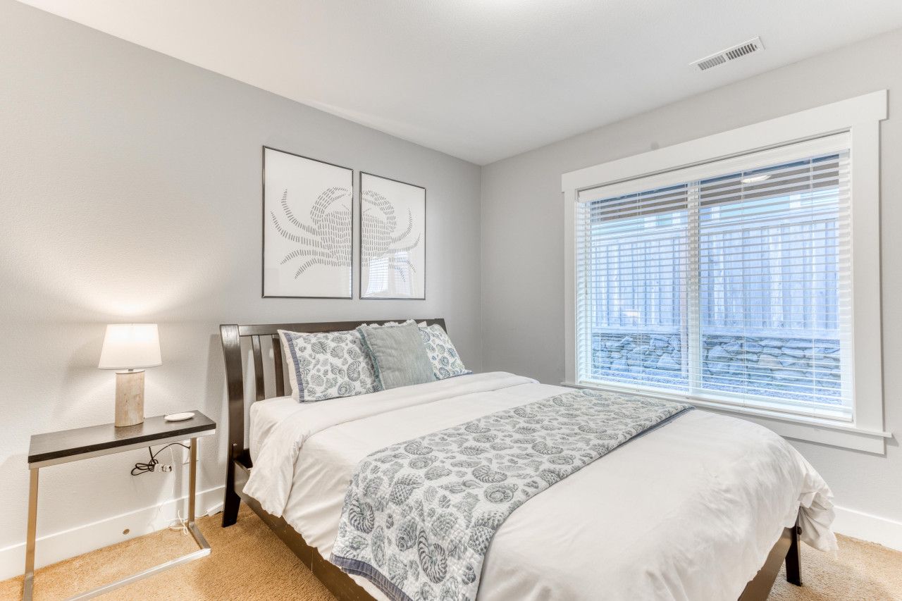 A bedroom with a bed, bedside table, lamp, and a window with blinds.