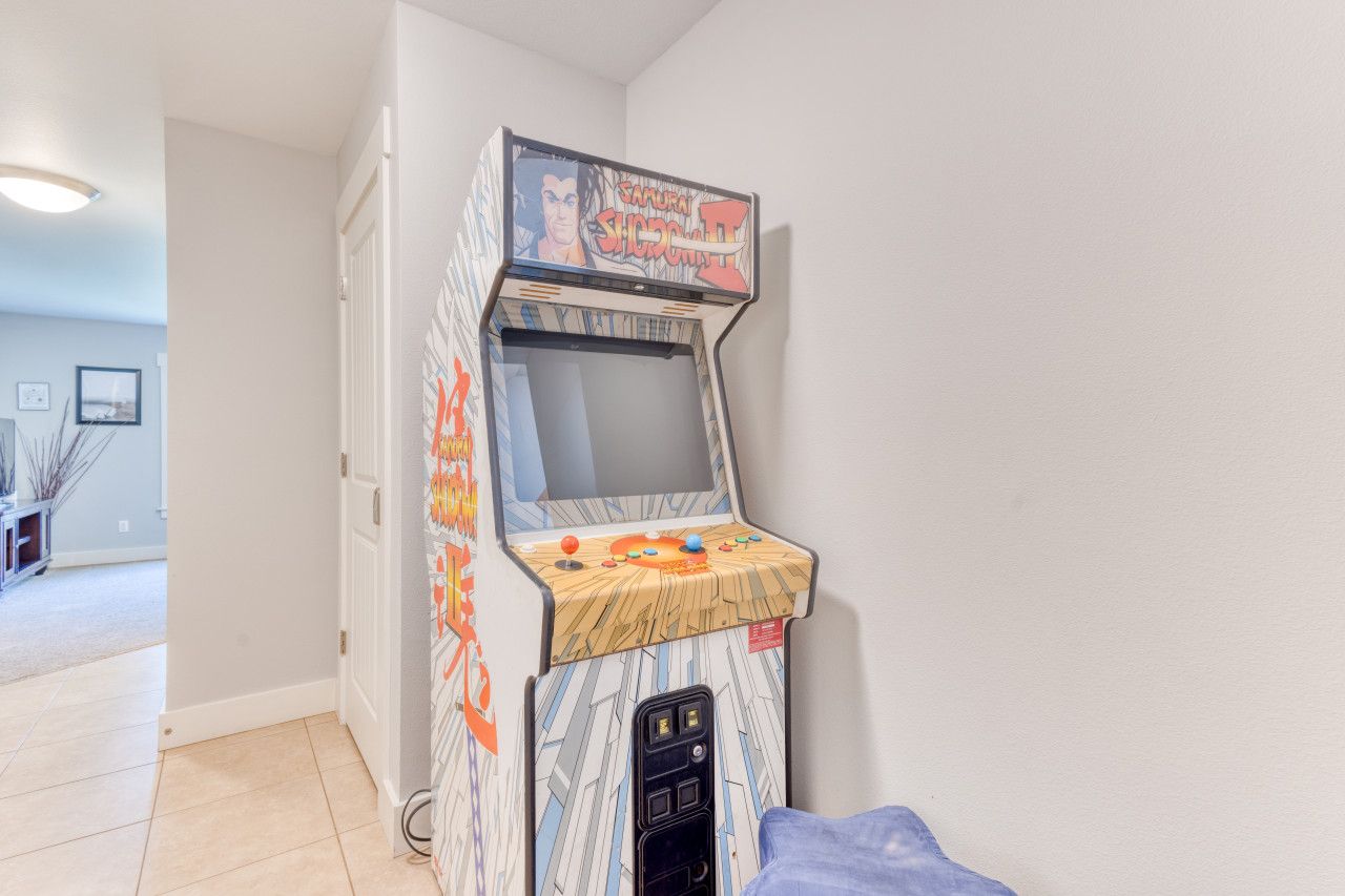 Una macchina arcade vintage con schermo e pannello di controllo, situata in una stanza con pavimento piastrellato e una porta.