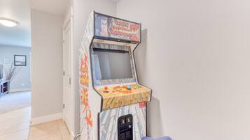 Una macchina arcade vintage con schermo e pannello di controllo, situata in una stanza con pavimento piastrellato e una porta.