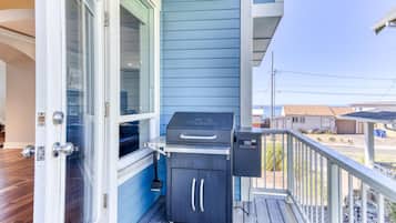 A balcony with a barbecue grill, a small cabinet, and a door leading to the interior.