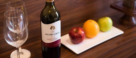 A bottle of Jacob's Creek wine, a wine glass, and a plate with an apple, an orange, and a green apple on a wooden table.