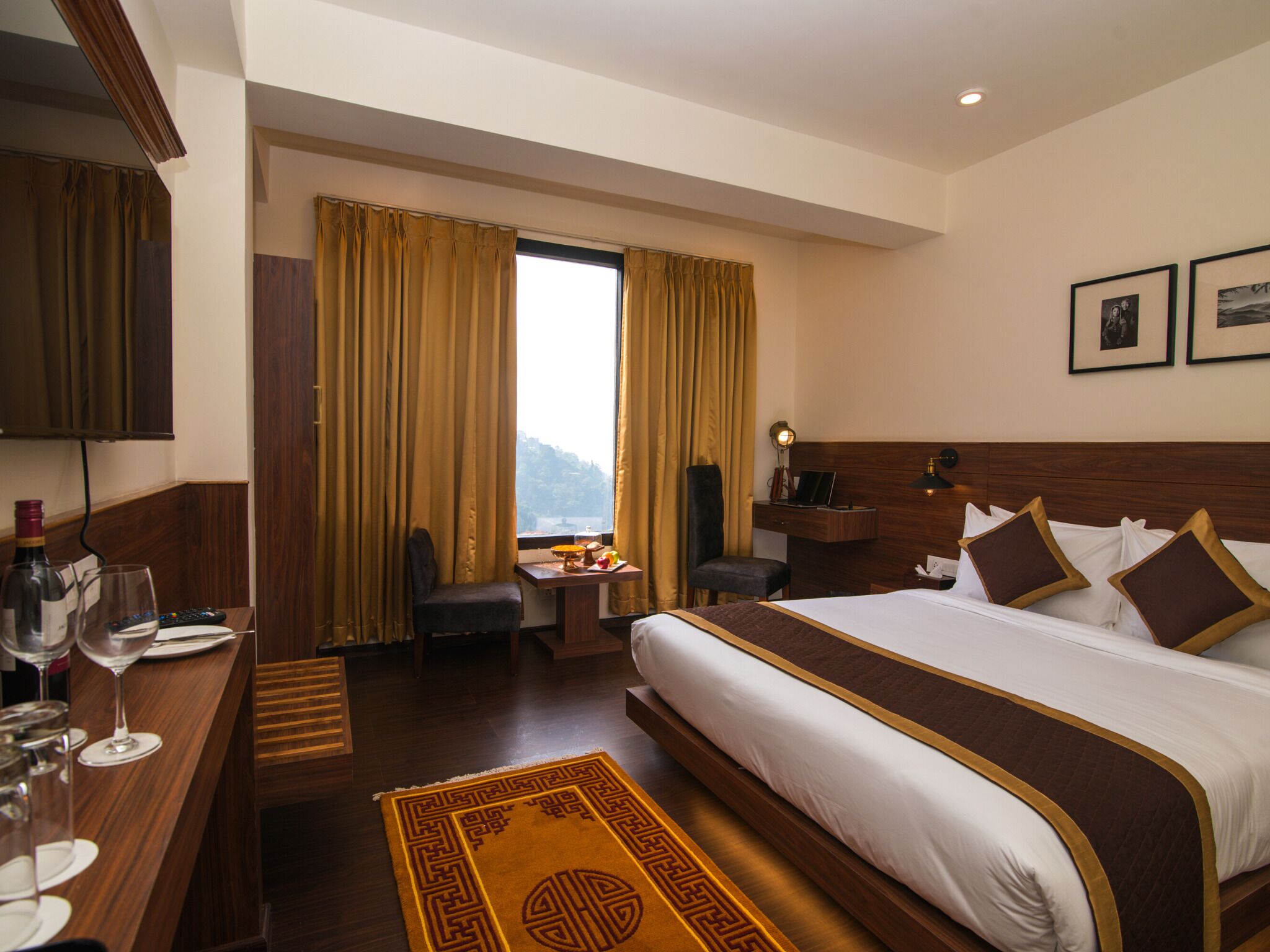 A hotel room with a large bed, a desk with a chair, a small table with a laptop, and a window with curtains.