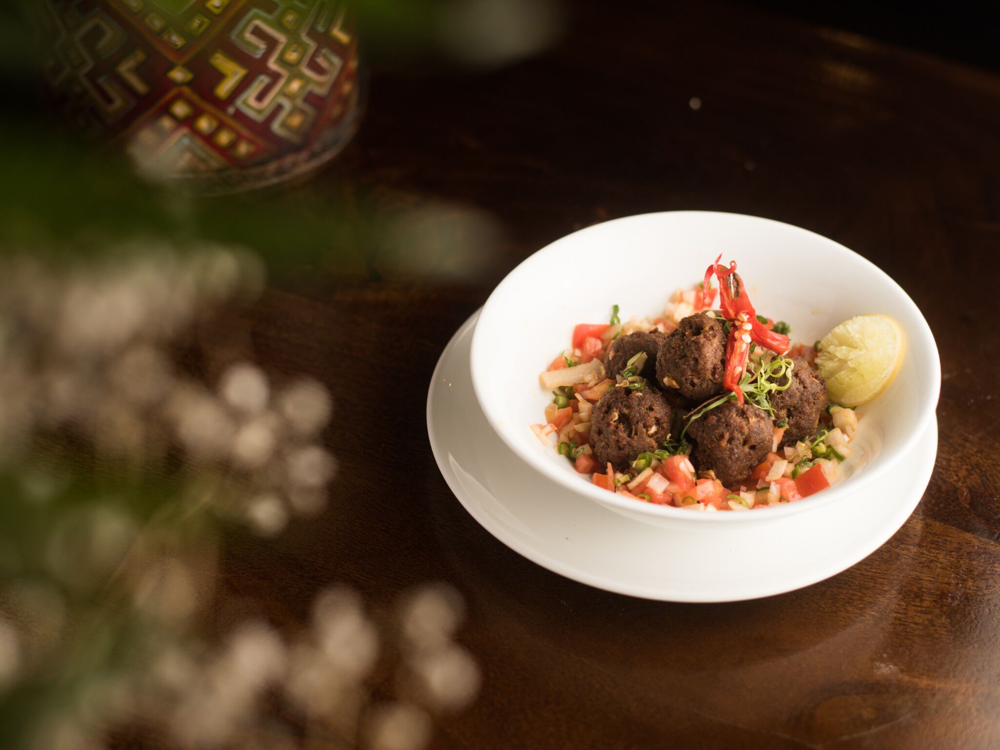 Un bol de boulettes de viande accompagnées de légumes et d’une tranche de citron, posé sur une table en bois.
