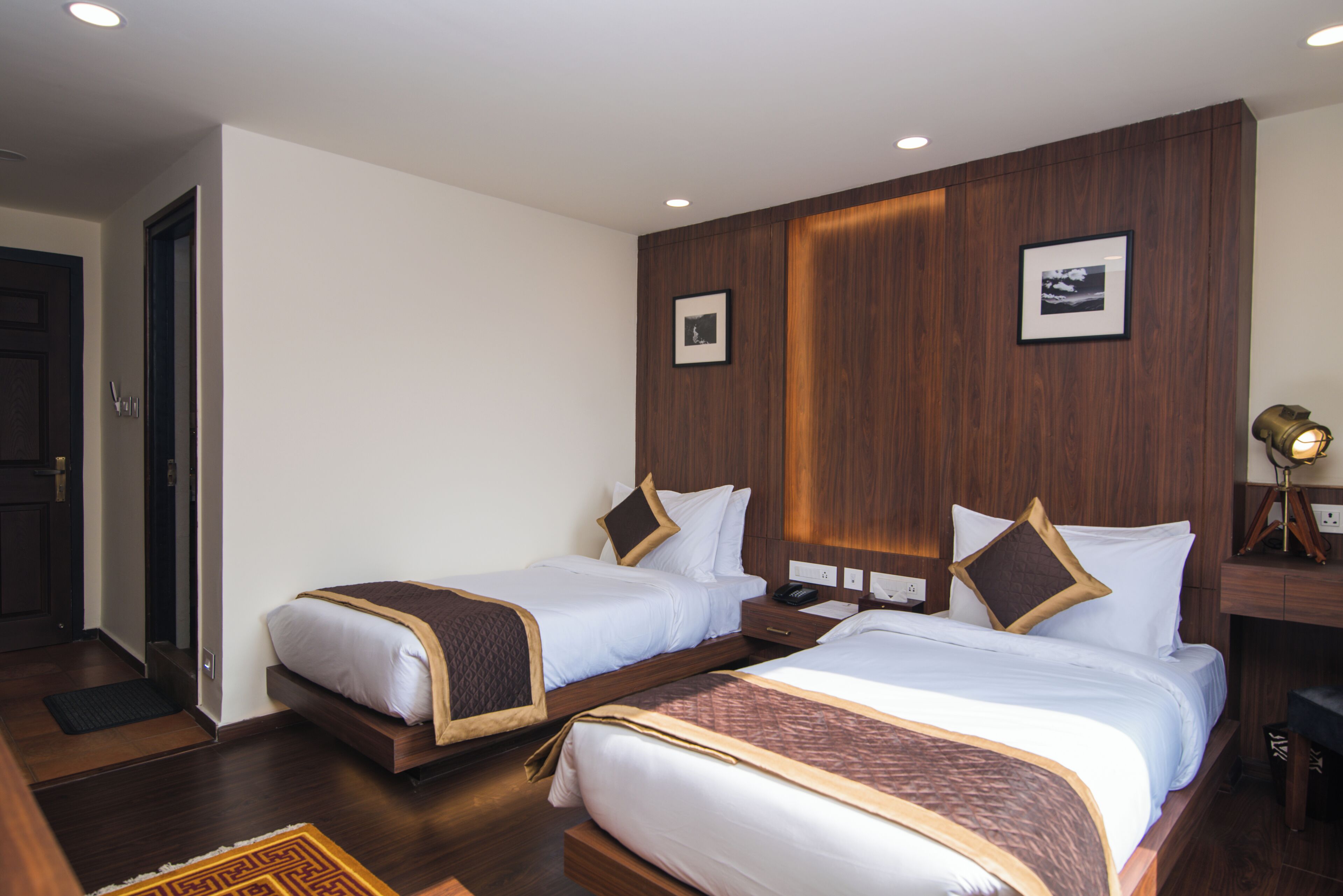 Una habitación de hotel con dos camas, paneles de madera en las paredes y un pequeño escritorio con lámpara.