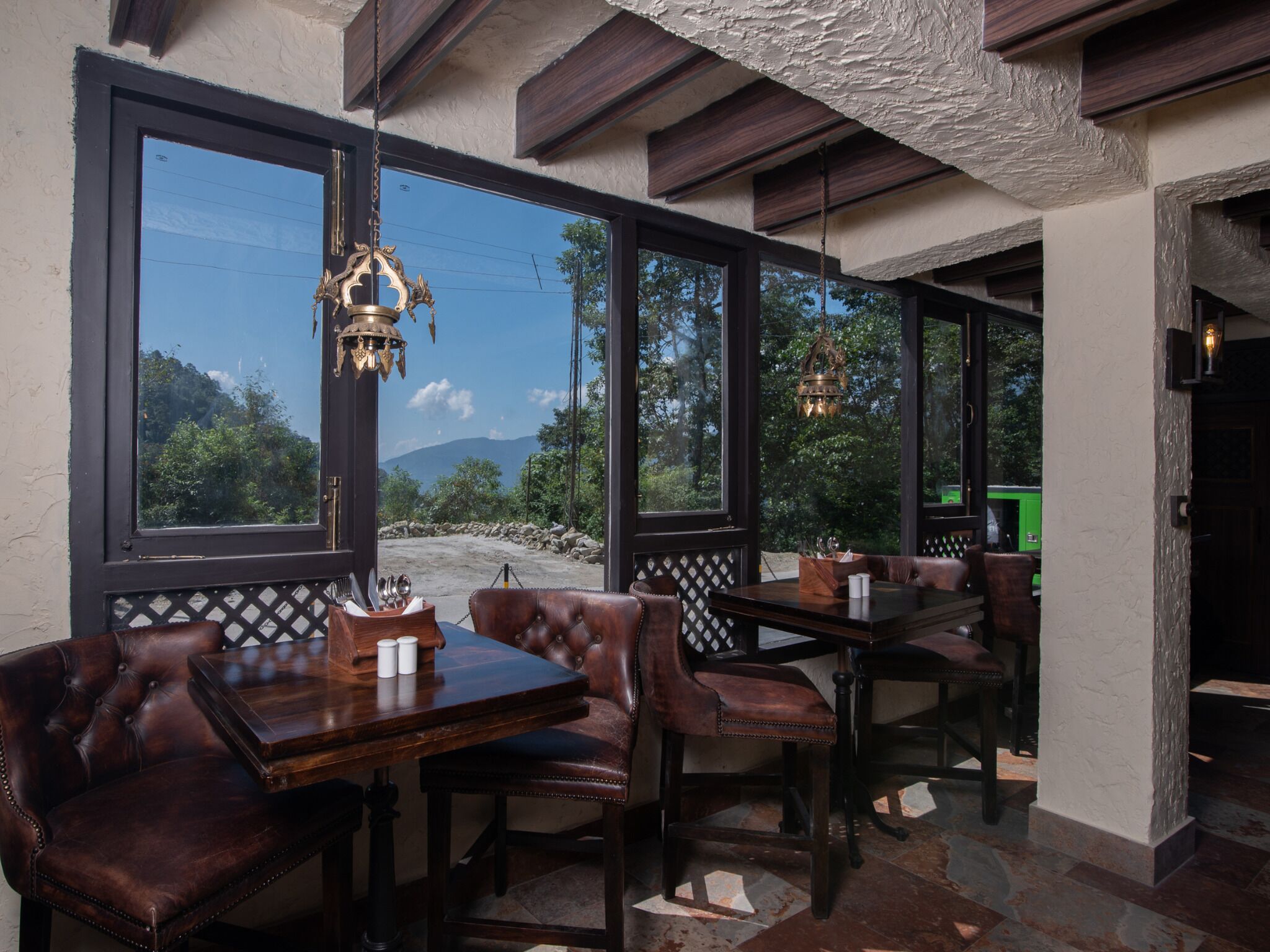 A restaurant with wooden tables and leather chairs, large windows with a view of trees and mountains, and hanging lanterns.