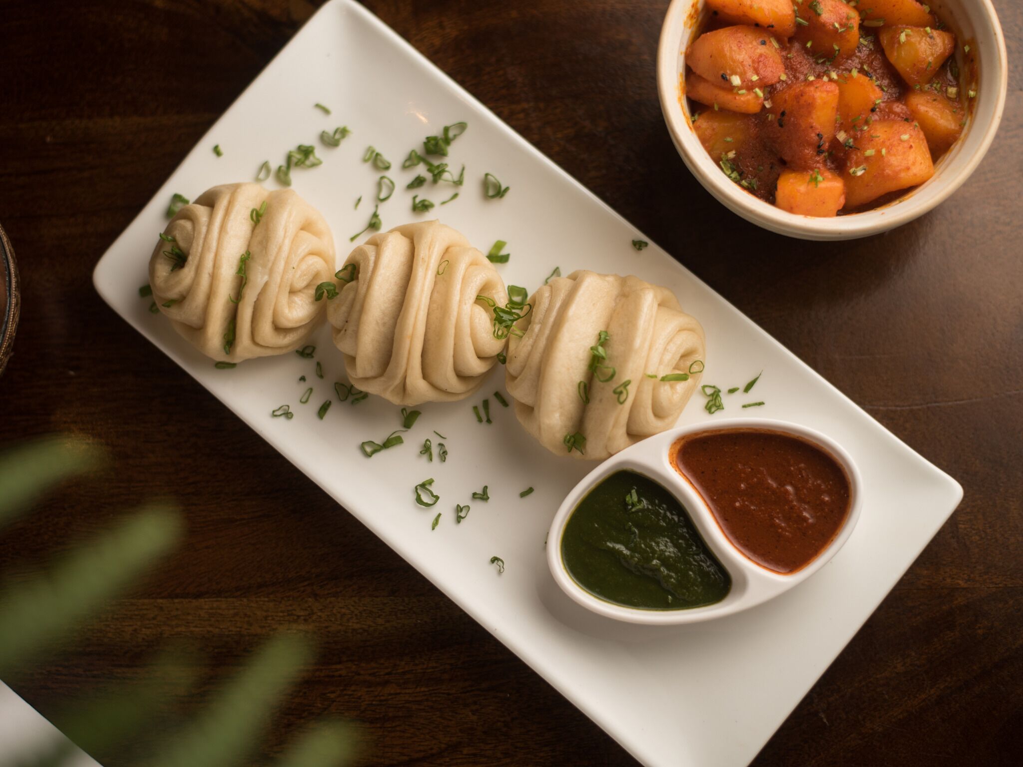 A plate with three dumplings, a bowl of sauce, and a bowl of vegetables.