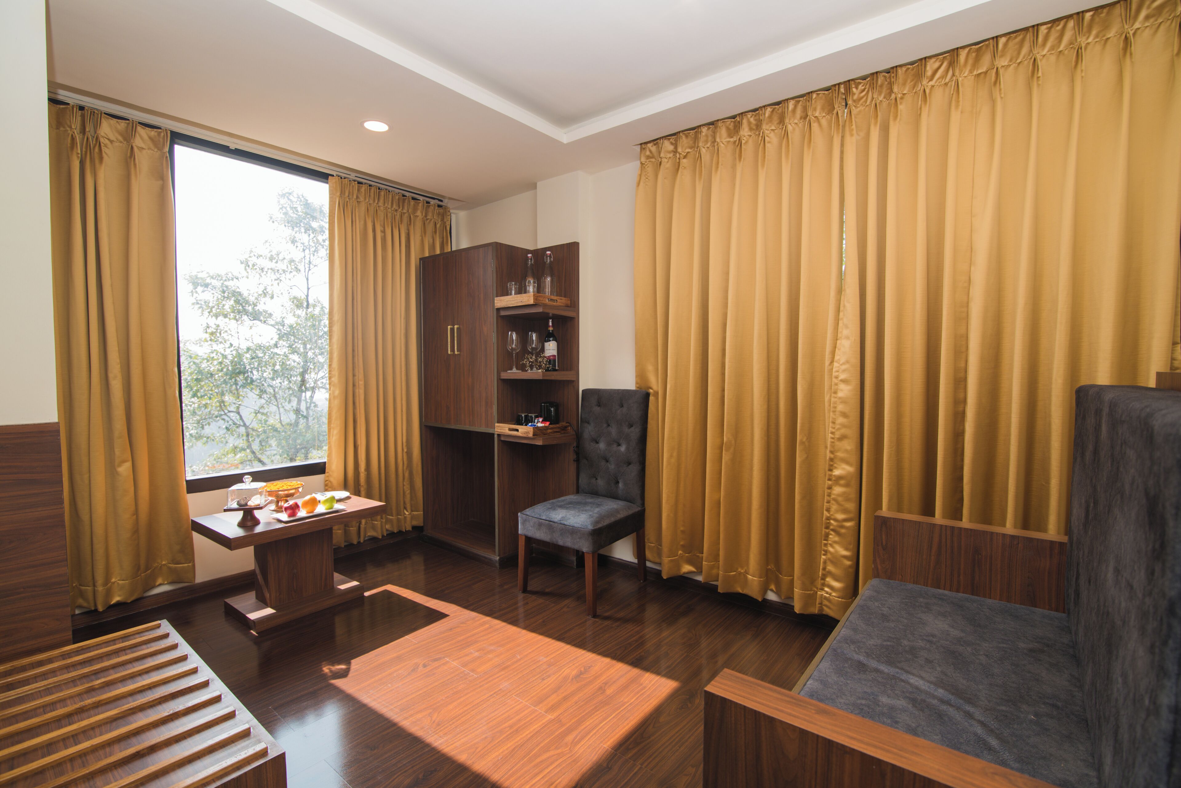 A room with a wooden floor, a sofa, a chair, a small table with a lamp, and a cabinet with shelves.