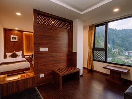 Une chambre d’hôtel avec un lit en bois, un banc, une petite table et une grande fenêtre donnant sur un paysage montagneux.