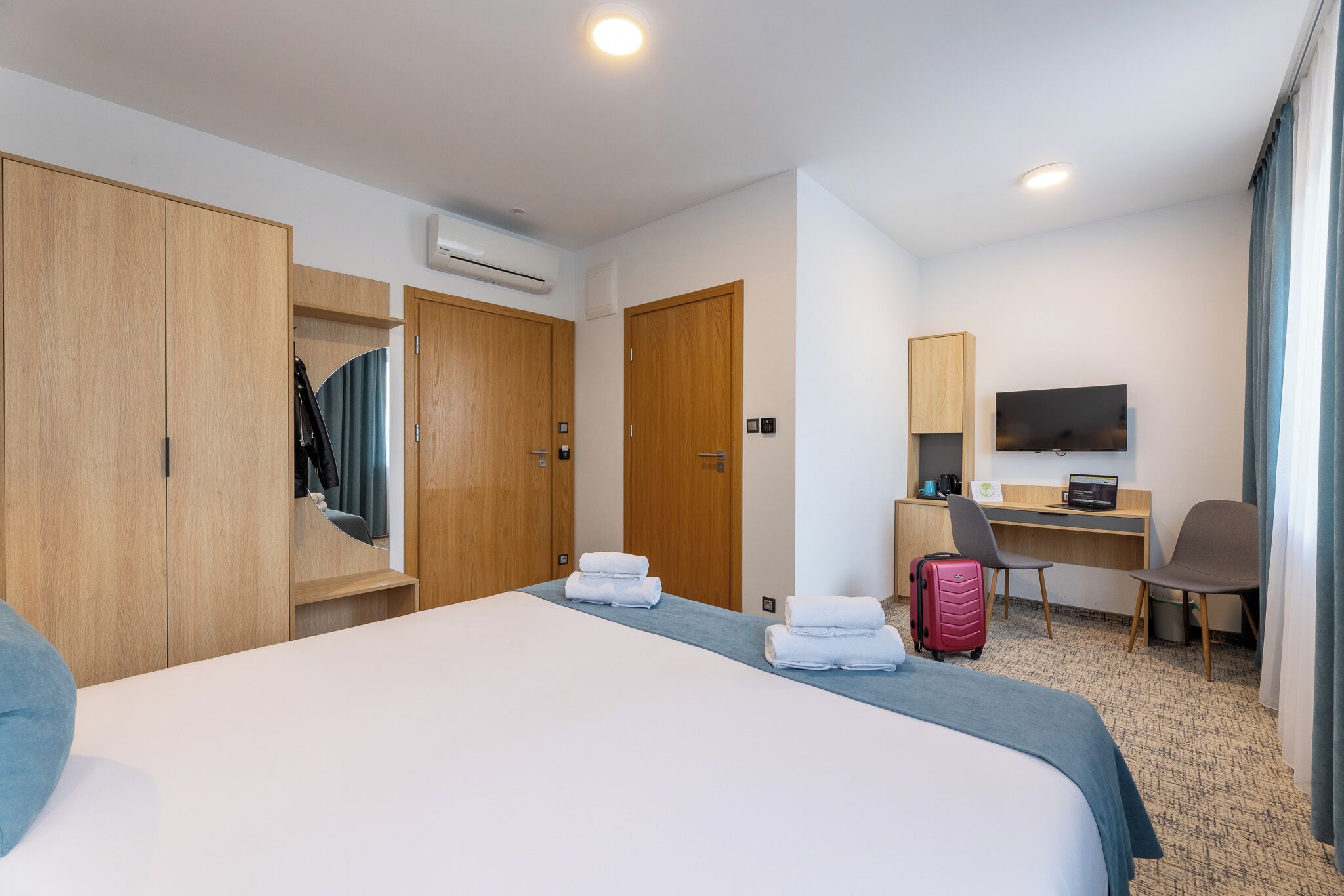 A hotel room with a large bed, a desk, a chair, a television, and a wardrobe.