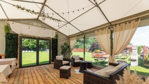 An indoor patio area with wicker furniture, a wooden floor, and a view of a garden through glass doors.