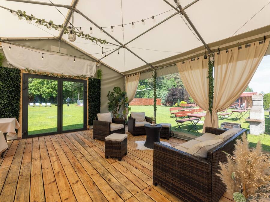 An indoor patio area with wicker furniture, a wooden floor, and a view of a garden through glass doors.