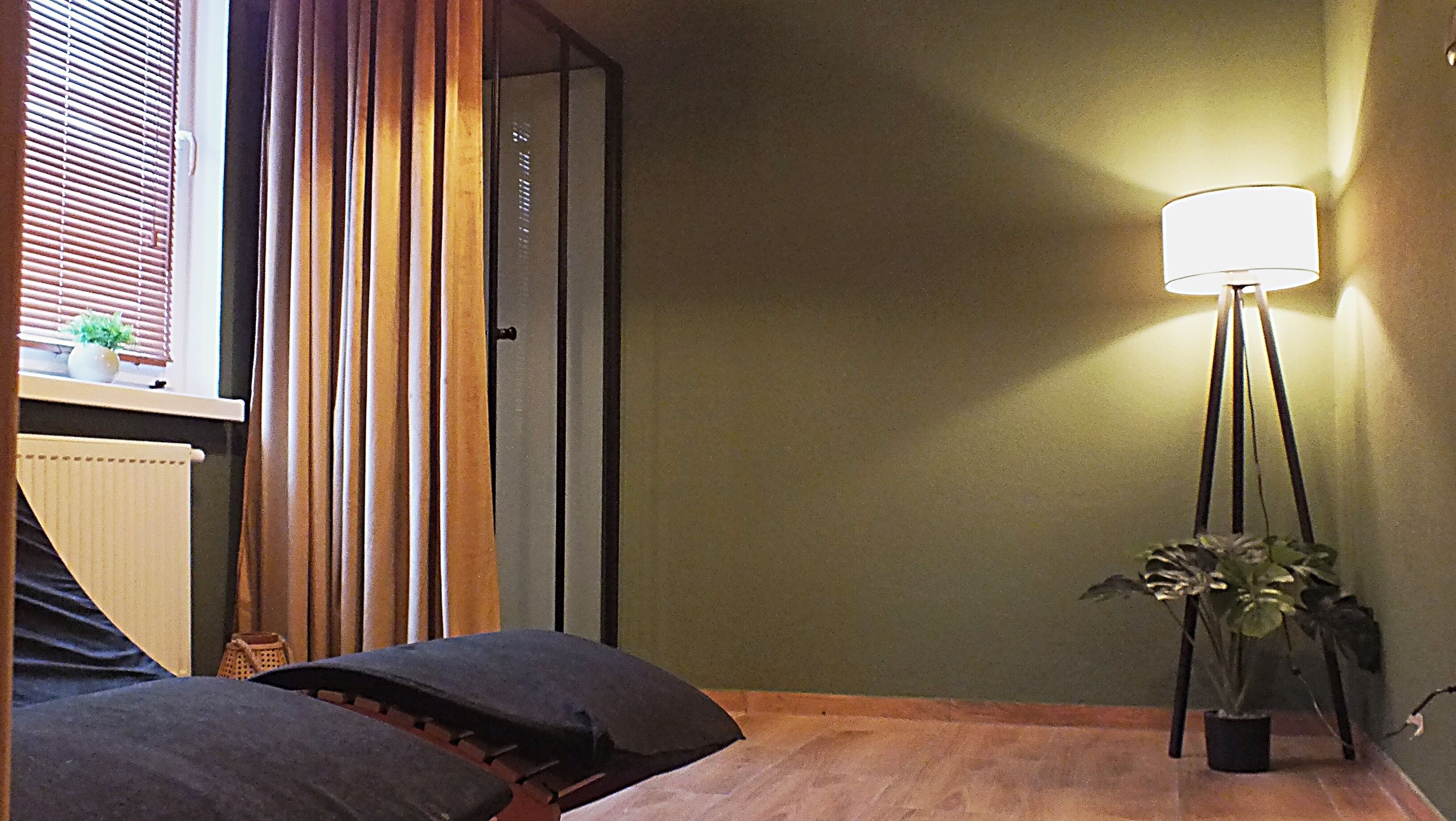 A room with a bed, a standing lamp, and a window with blinds.