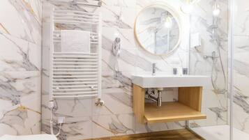 A modern bathroom with a marble floor, a wooden vanity, a white sink, a towel rack, a mirror, and a shower area.