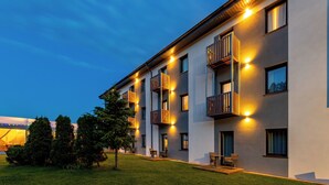 A modern multi-story building with balconies, outdoor seating, and a well-maintained lawn. - Awilla (Ustka)
