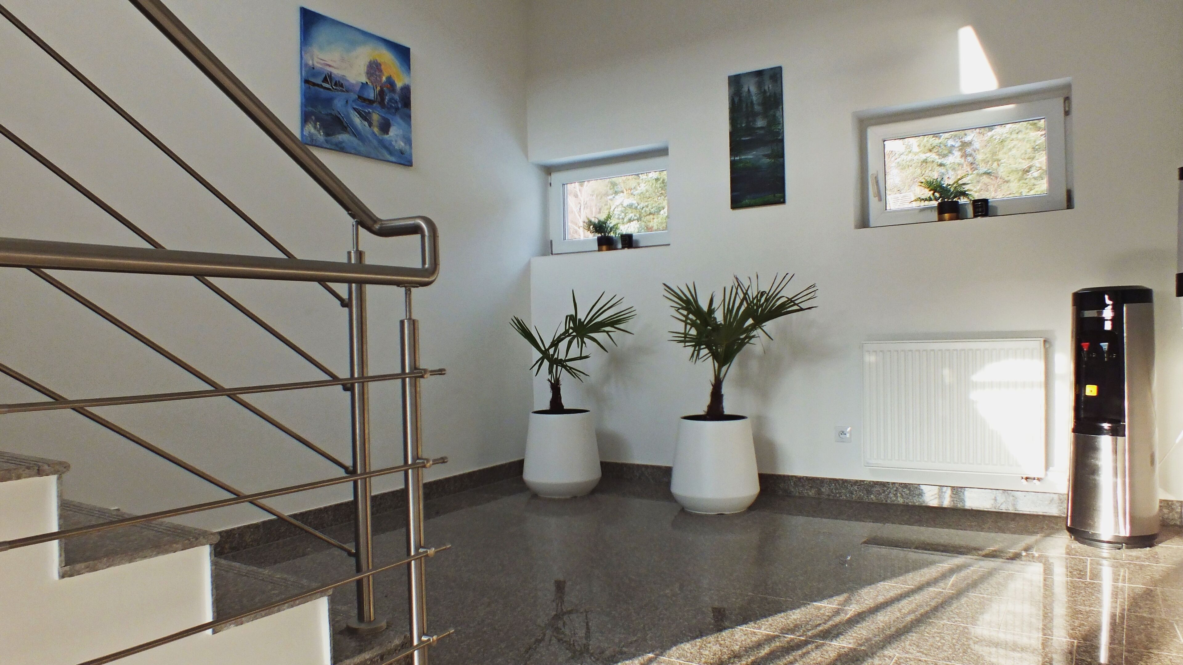 Un interior moderno con una escalera, plantas en macetas, radiadores y obras de arte en las paredes.