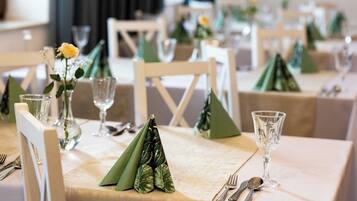 A dining table set with green napkins, clear glassware, and a vase with a yellow flower.