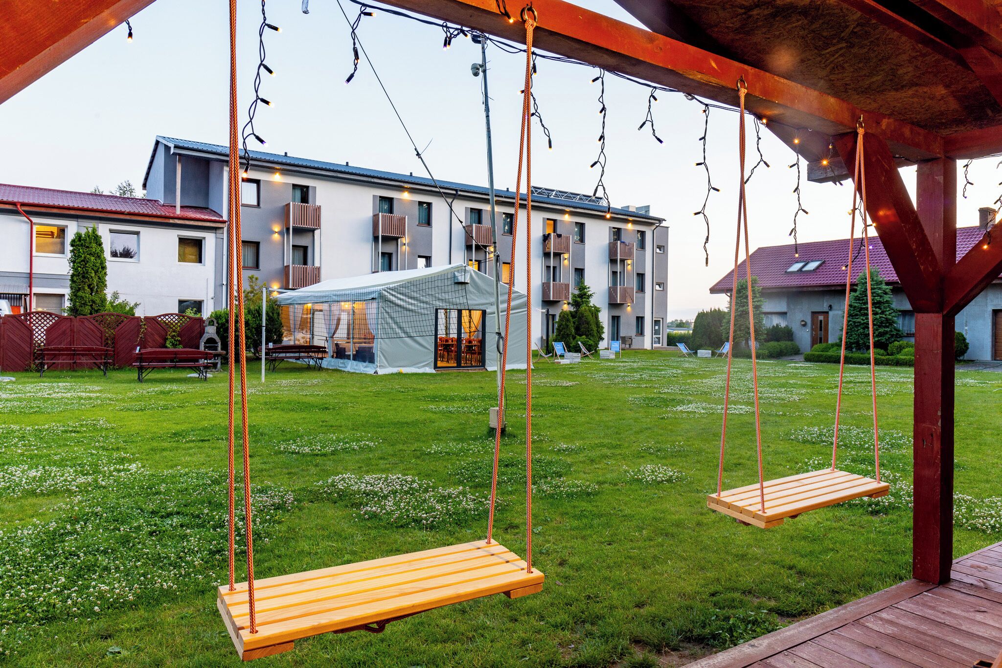 A wooden swing set in a grassy yard with a building in the background.