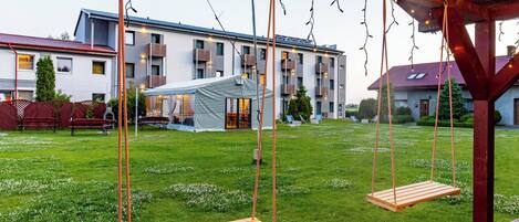A wooden swing set in a grassy yard with a building in the background.