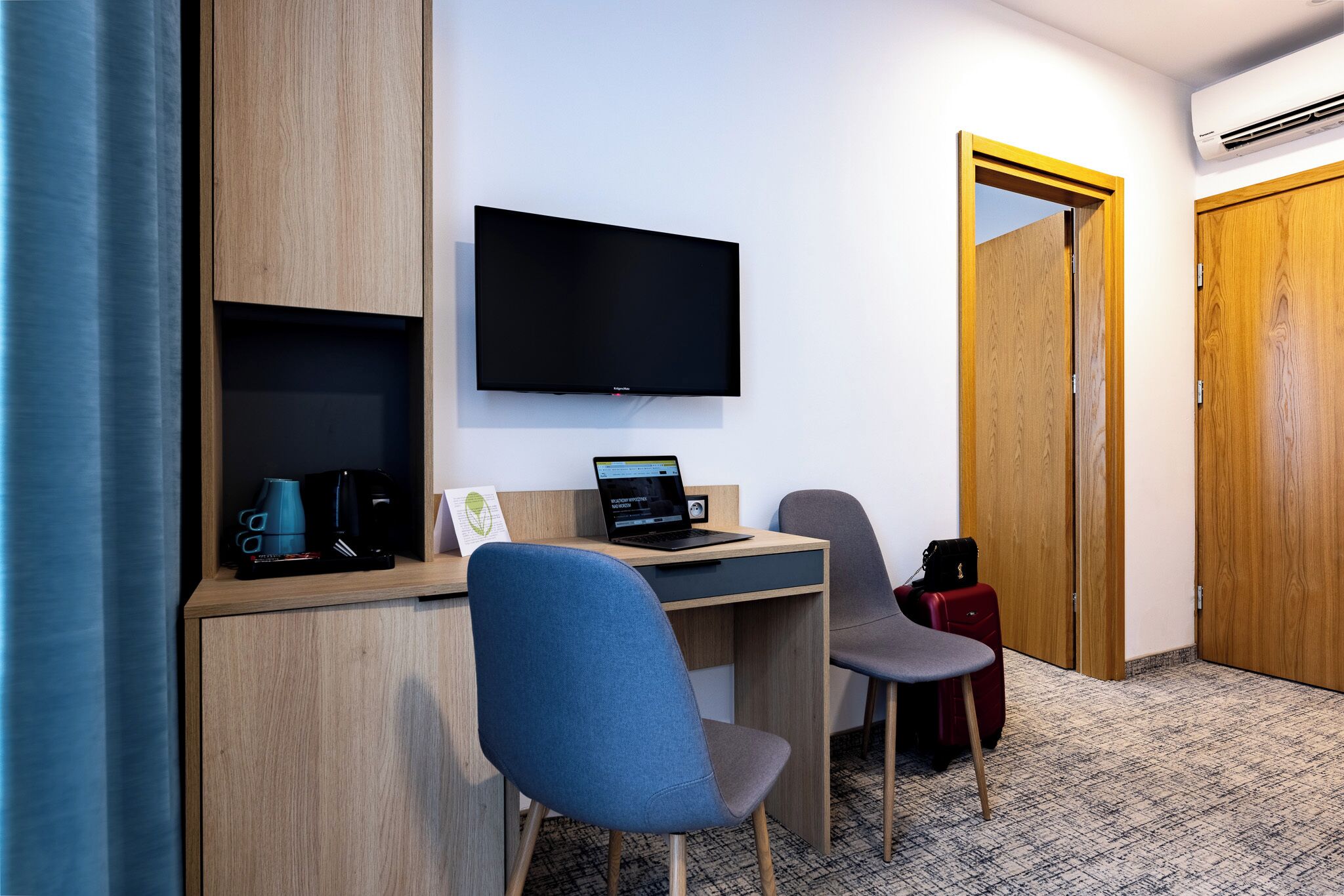 A hotel room with a desk, a laptop, a television, and a chair.