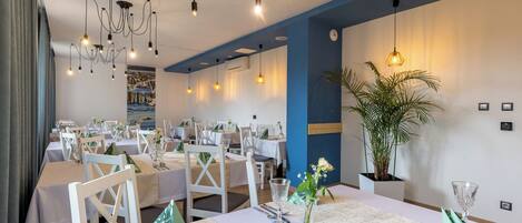 A restaurant with multiple tables set for dining, featuring white tablecloths, clear glassware, and a variety of chairs.