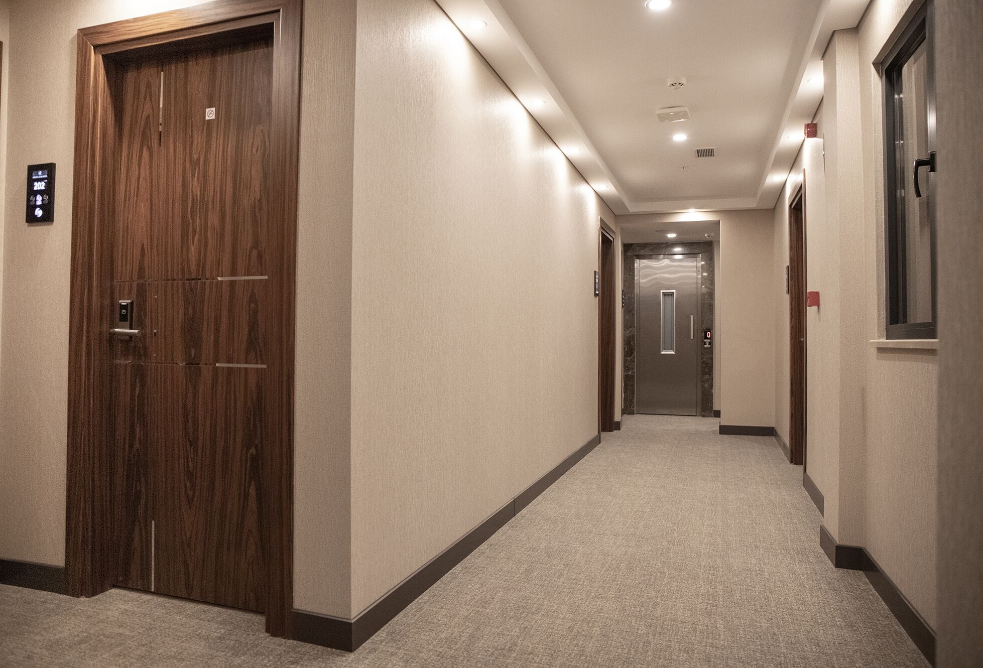 A hotel hallway with wooden doors, carpeted floors, and a modern ceiling design.