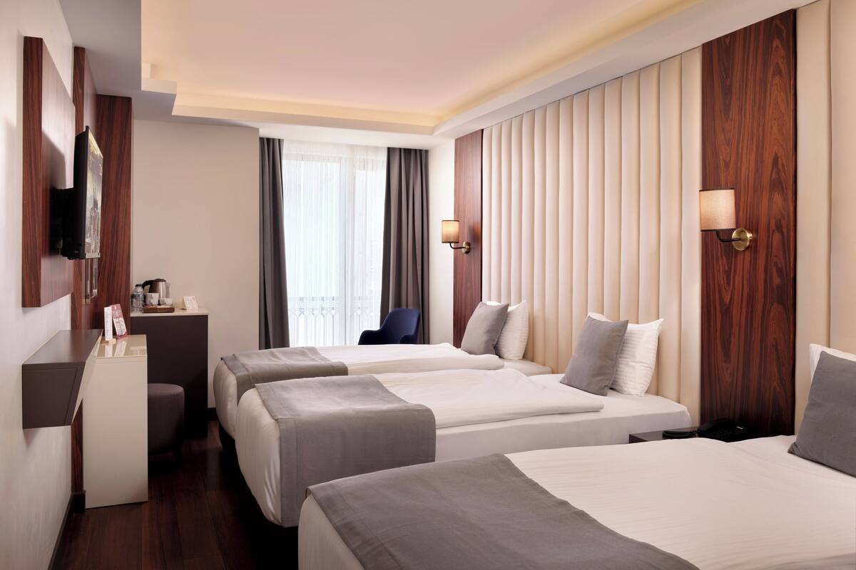A hotel room with two beds, a desk, a chair, a TV, and a window with curtains.