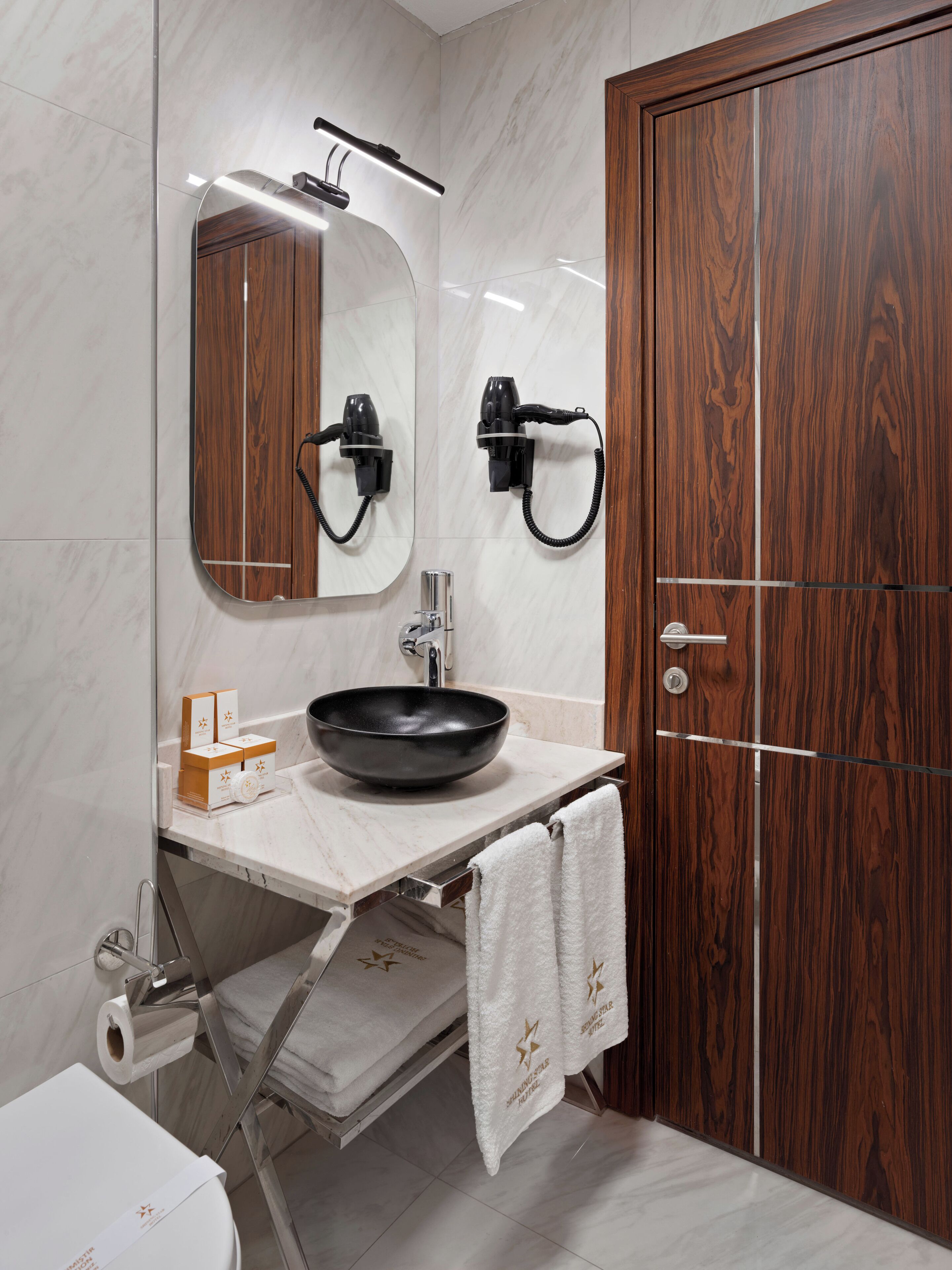 A bathroom with a wooden door, a mirror, a sink with a black basin, and a towel rack.