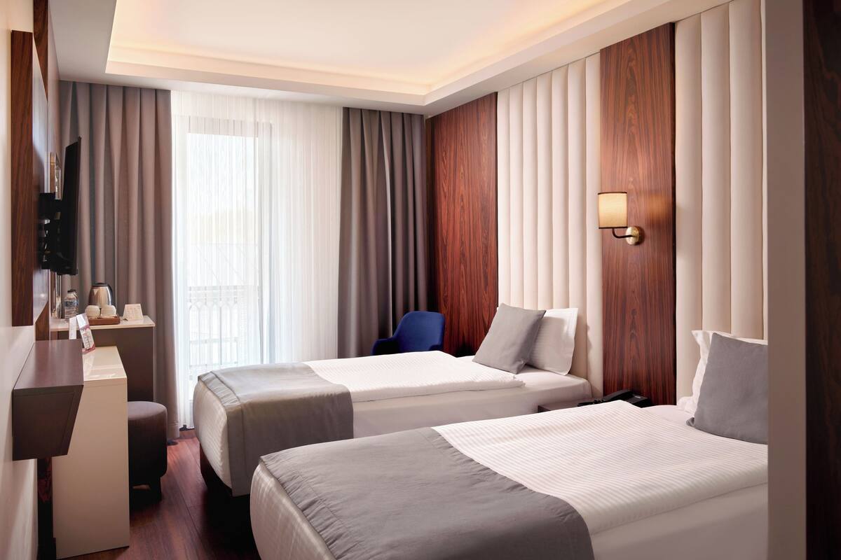 A hotel room with two beds, a desk, a chair, a TV, and a window with curtains.
