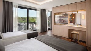A hotel room with two beds, a large window with a view of greenery, a balcony, and a desk with a TV and a mirror. - Shining Star Hotel (Istanbul)