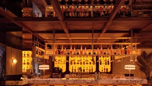 A bar area with a marble countertop, multiple wine glasses, and a variety of bottles. There are four bar stools with patterned upholstery. The ceiling features exposed wooden beams and a chandelier. - Shining Star Hotel (Istanbul)