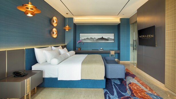 Una habitación de hotel moderna con una cama grande, mesitas de noche, un televisor y un cuadro en la pared.