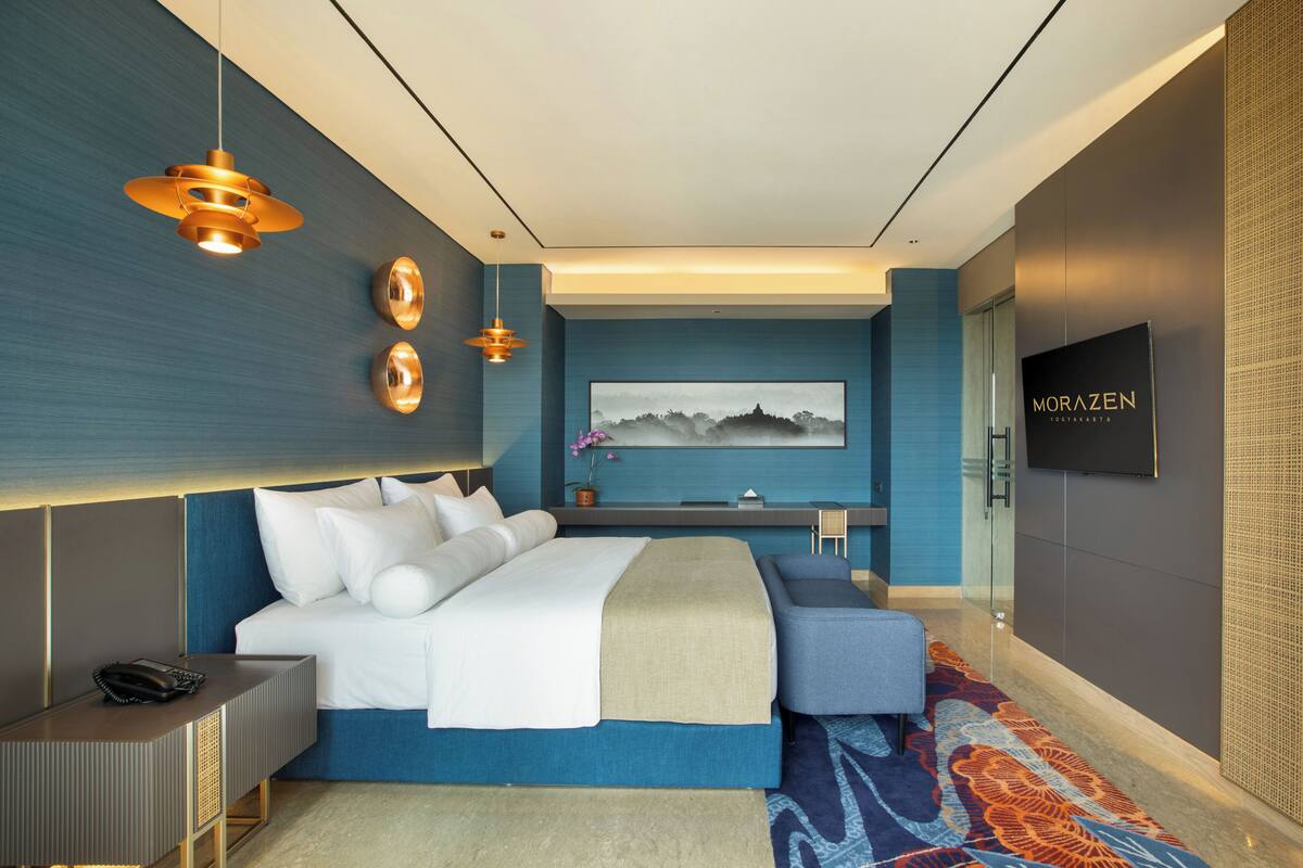 A modern hotel room with a large bed, bedside tables, a TV, and a painting on the wall.