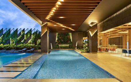 A modern indoor pool with a clear view of the sky, surrounded by lounge chairs and a reception area.
