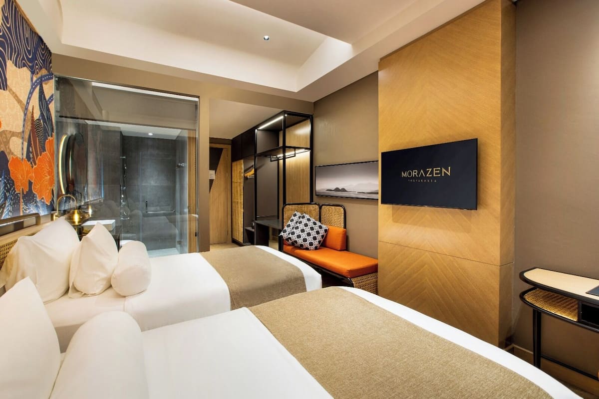 A hotel room with two beds, a seating area, a TV, and a large window.
