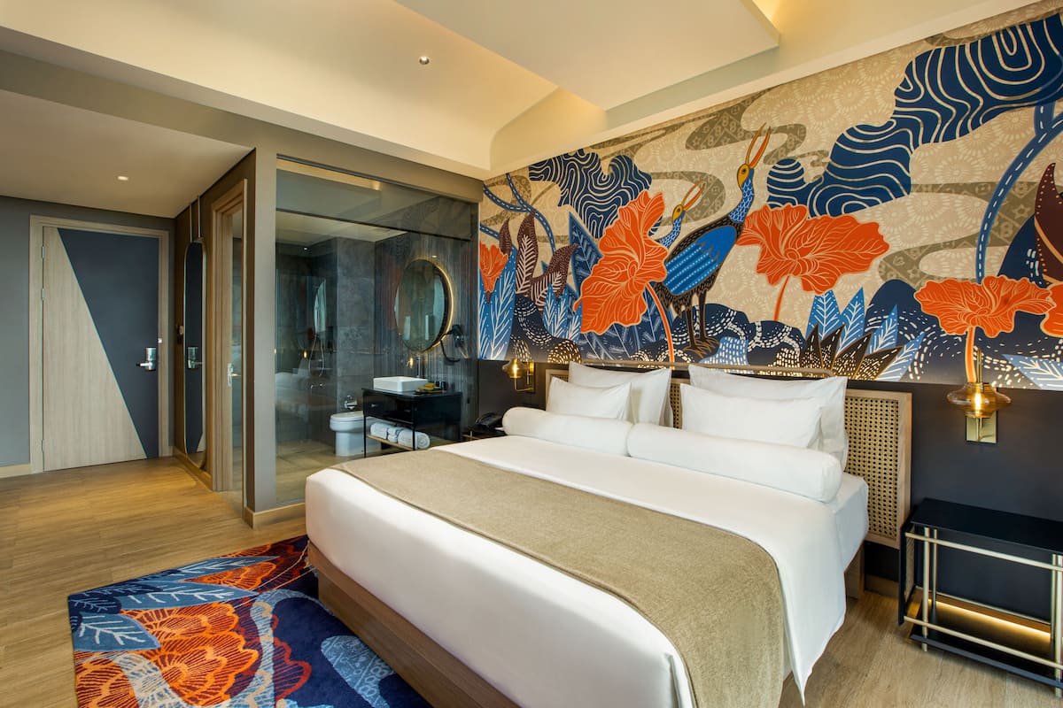 A modern hotel room with a large bed, a glass shower enclosure, and a vibrant floral wall mural.
