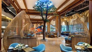 Een ruime lobby met hoge plafonds, een centrale boom en zithoeken met tafels en stoelen.
