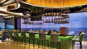 Een bar met uitzicht op de oceaan, barstoelen en een bord waarop 'MORAZEN YOGYAKARTA' staat.