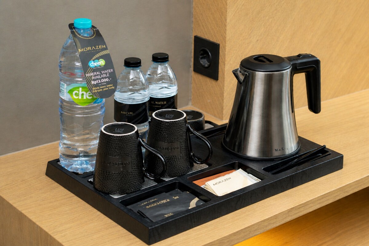 A hotel room's minibar setup with mineral water, coffee mugs, a kettle, and a tea bag.