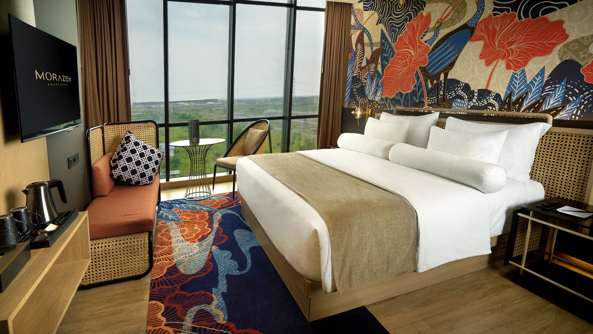 Habitación de hotel con una cama grande, televisión, zona de estar con una silla y vistas al paisaje a través de amplios ventanales.