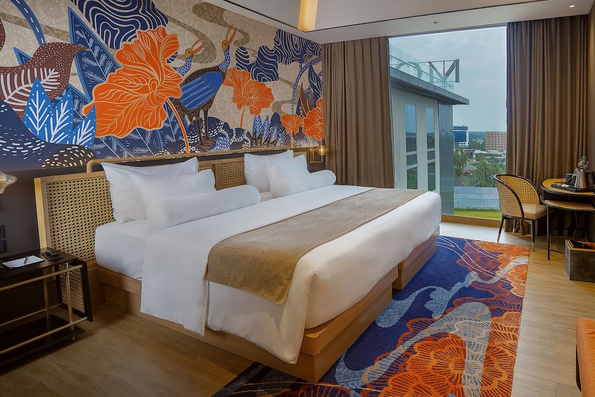 Habitación de hotel con una cama grande, un escritorio con silla, vistas a la ciudad y un mural decorativo.
