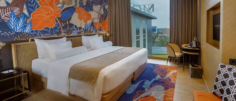 A hotel room with a large bed, a desk with a chair, a view of the city, and a decorative wall mural.