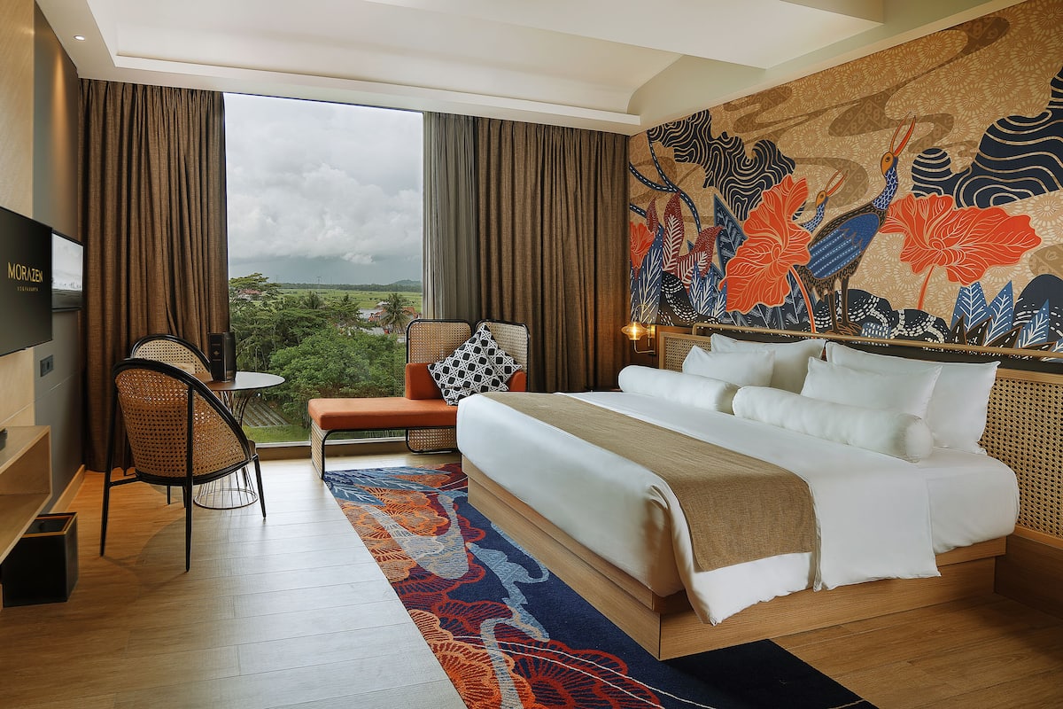 A hotel room with a bed, a desk with a TV, a chair, and a view of the outdoors.