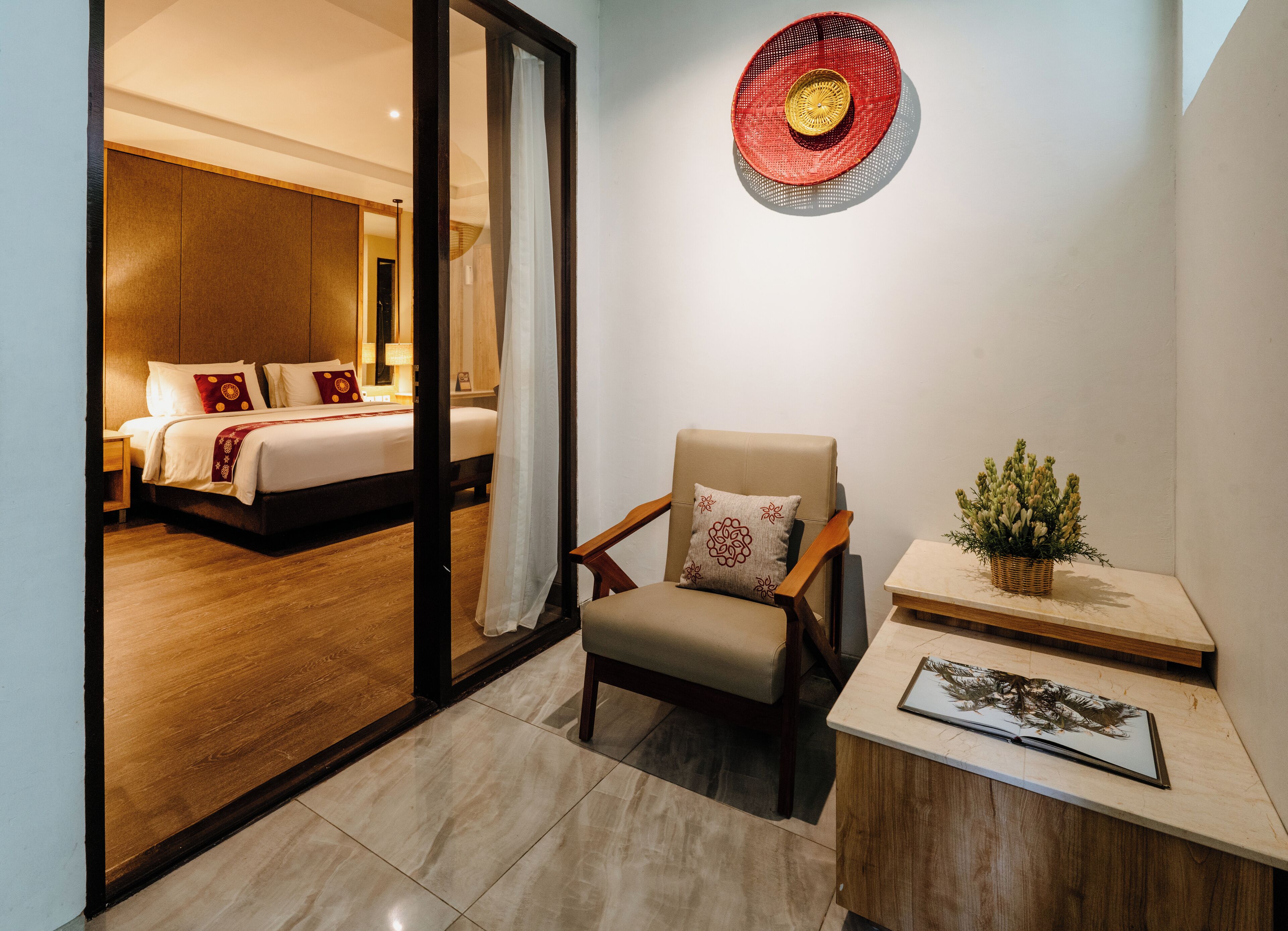 Habitació d'hotel amb llit, una cadira, una taula petita amb una planta i un objecte decoratiu penjat a la paret.