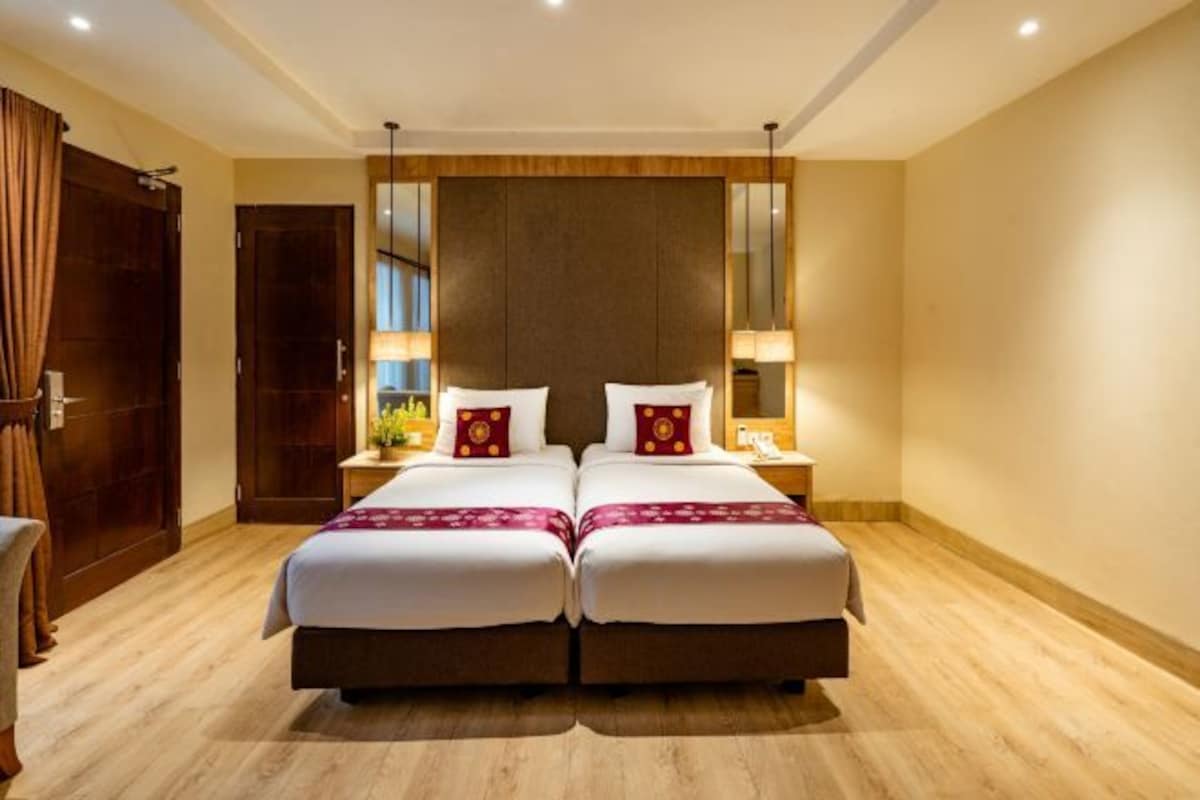 Una cama doble con cabecera de madera, dos mesitas de noche con lámparas y suelo de madera.