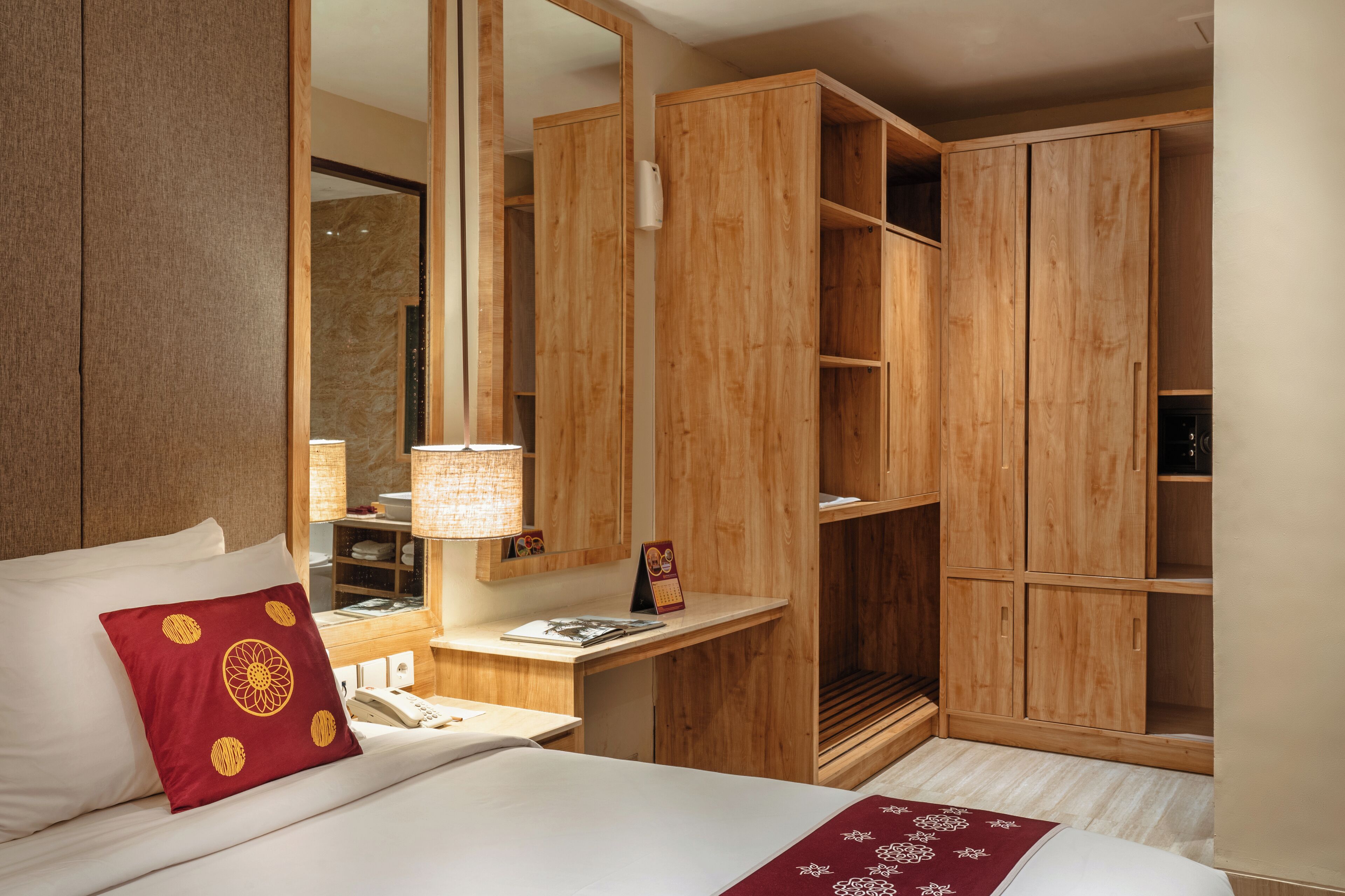 A hotel room with a bed, a wooden wardrobe, a nightstand with a lamp, and a mirror.
