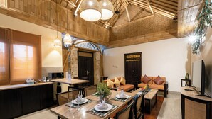 Un salón espacioso con techo de madera, una mesa de comedor con platos y vasos, un sofá con cojines y un televisor sobre un mueble.