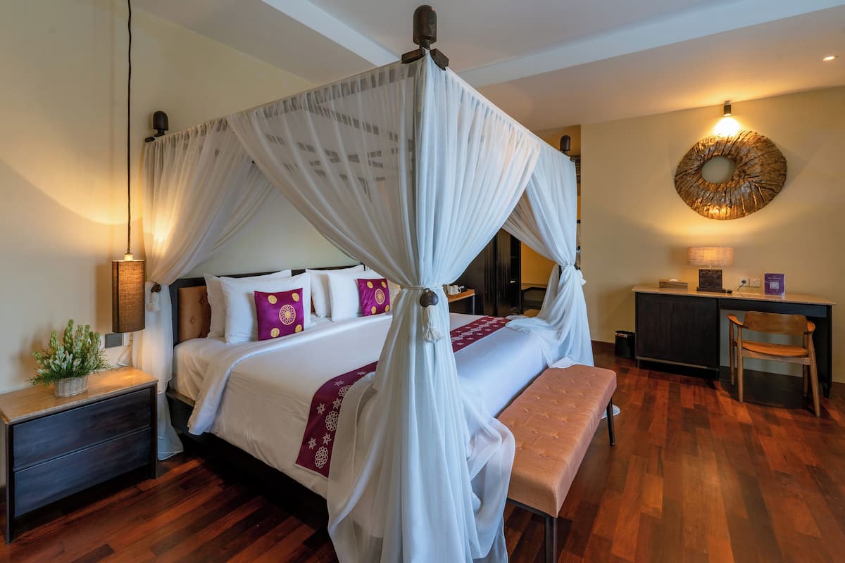 A four-poster canopy bed with a bench, bedside table, and lamp.