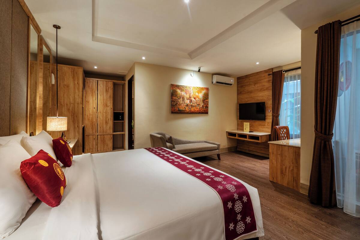 A hotel room with a large bed, a desk, a chair, a TV, and wooden paneling.