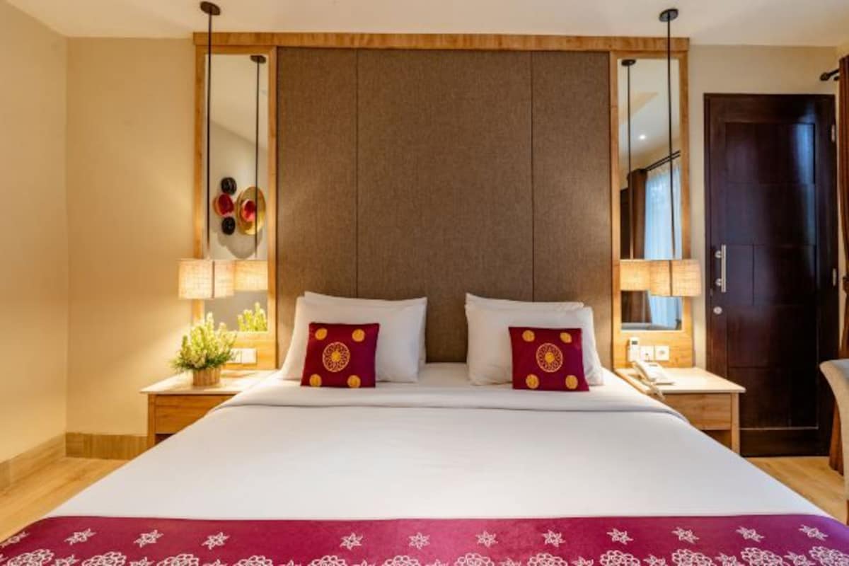 Una habitación de hotel con una cama grande, dos mesitas de noche, un espejo y una puerta.