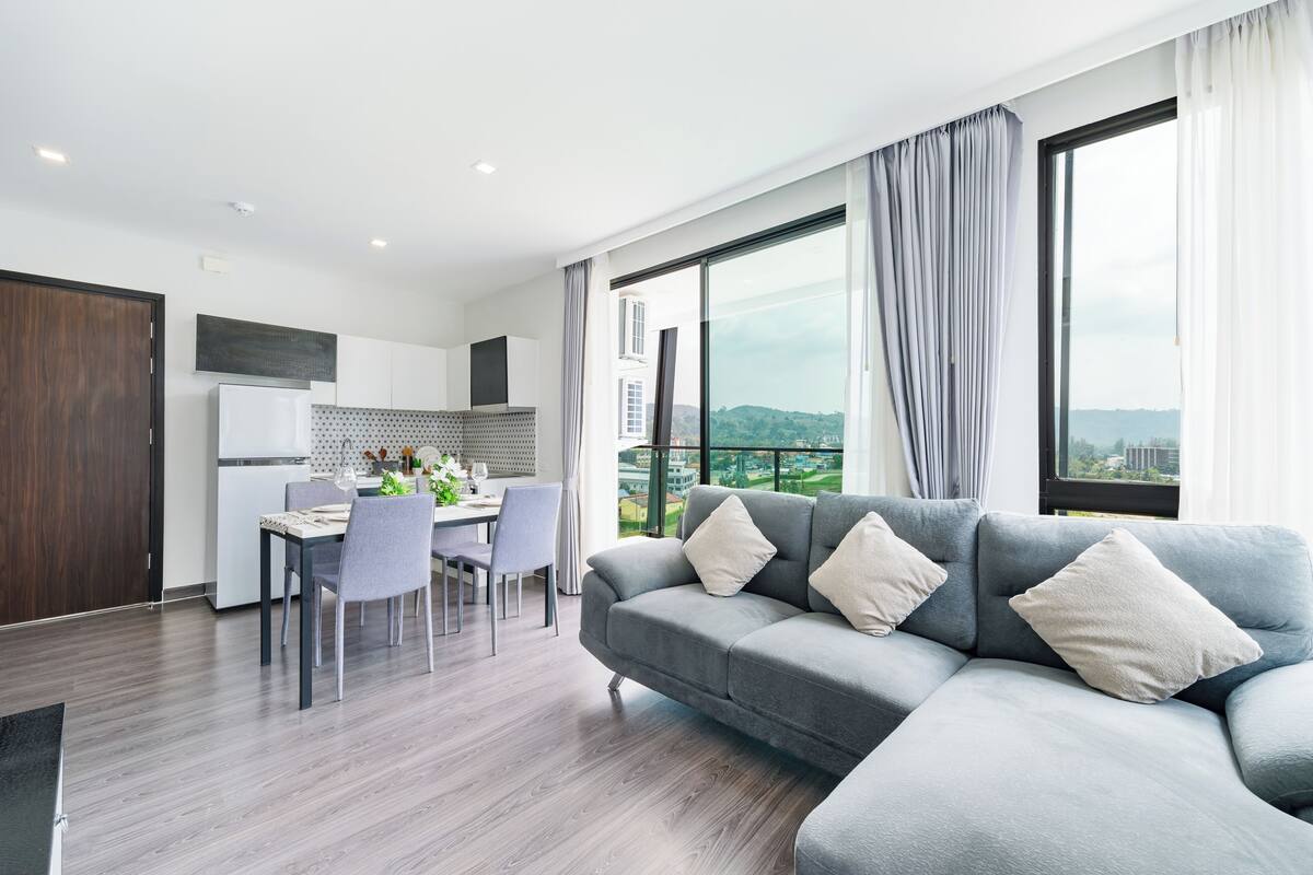 Ein modernes Wohnzimmer mit grauem Sofa, Essbereich und großen Fenstern mit Blick auf die Stadt.